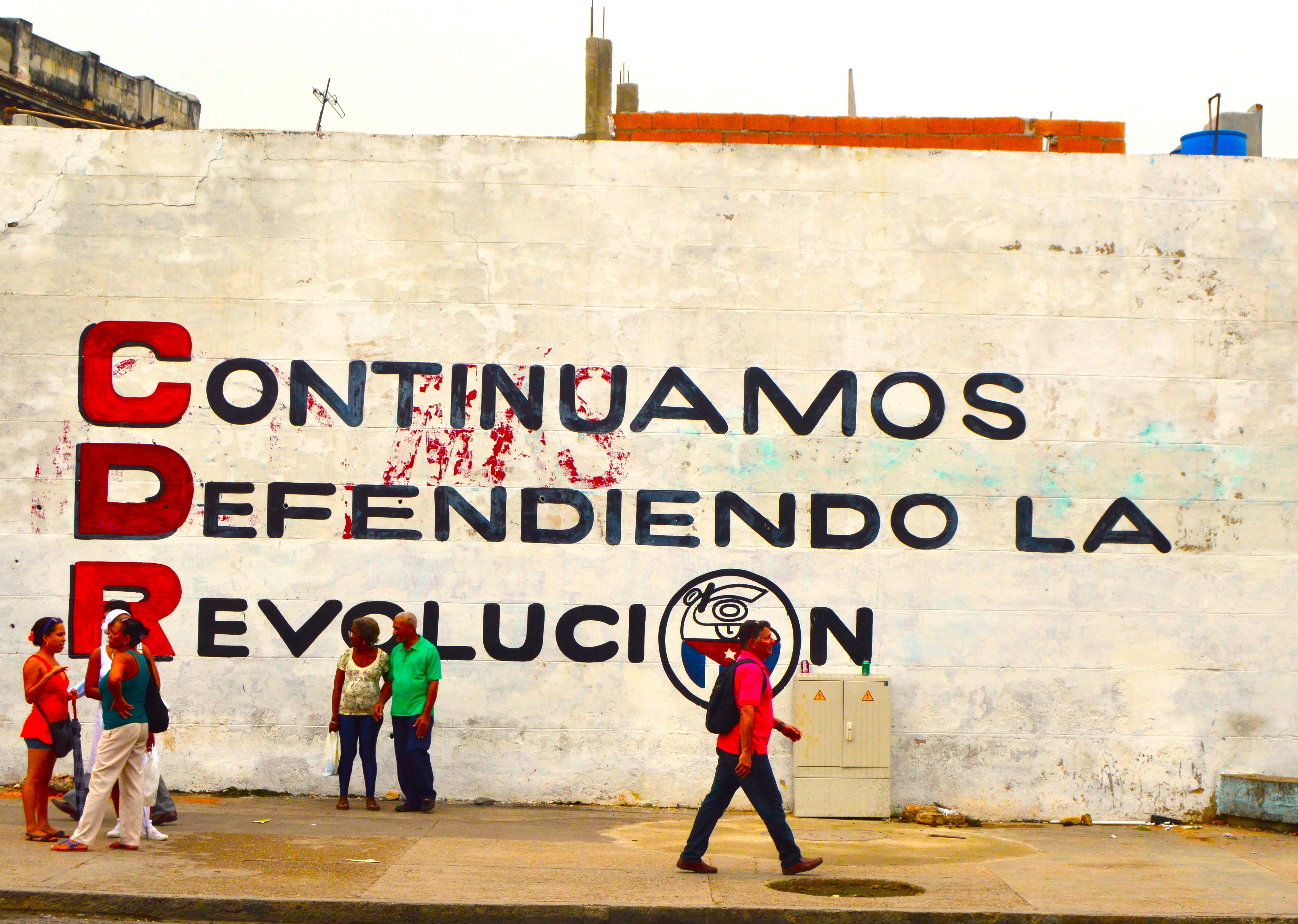 Transeúntes en La Habana con mural de fondo: Sigamos defendiendo la Revolución